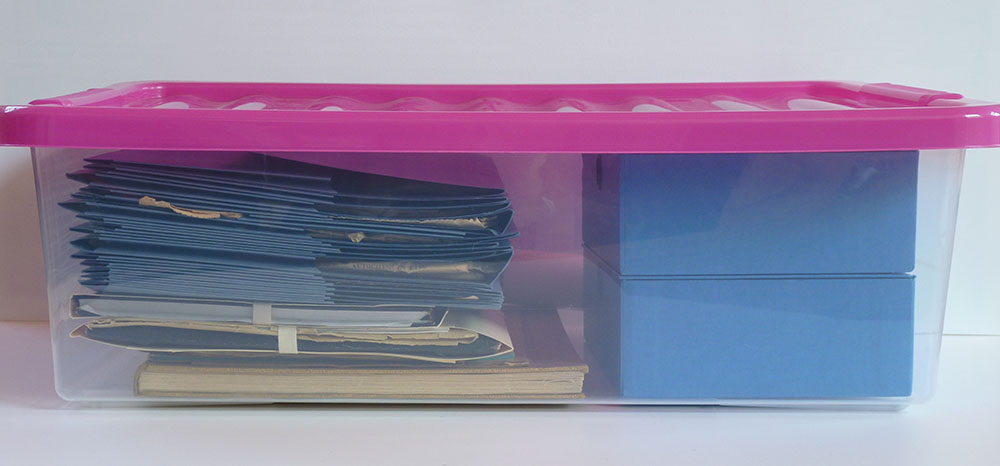 Photograph of a storage box containing folders and books stored flat.